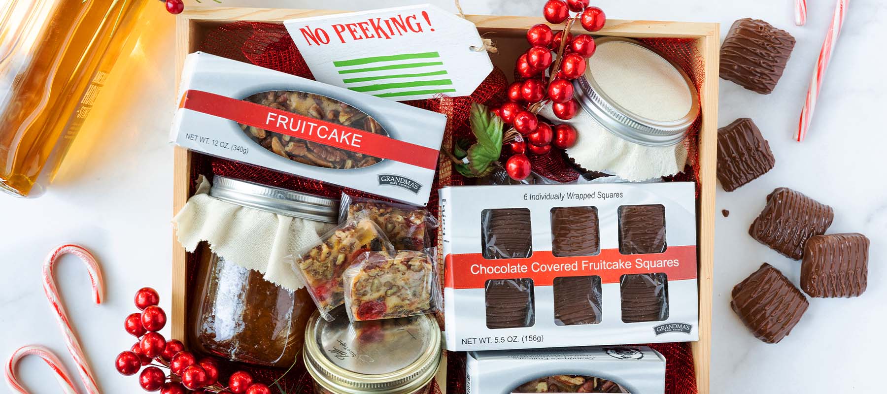 Overhead view of a wooden gift box containing a rectangular fruitcake, a box of chocolate covered fruitcake squares labeled